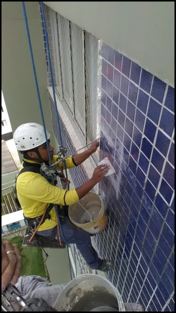 Profissional aplicando pastilhas azuis em fachada por acesso em altura